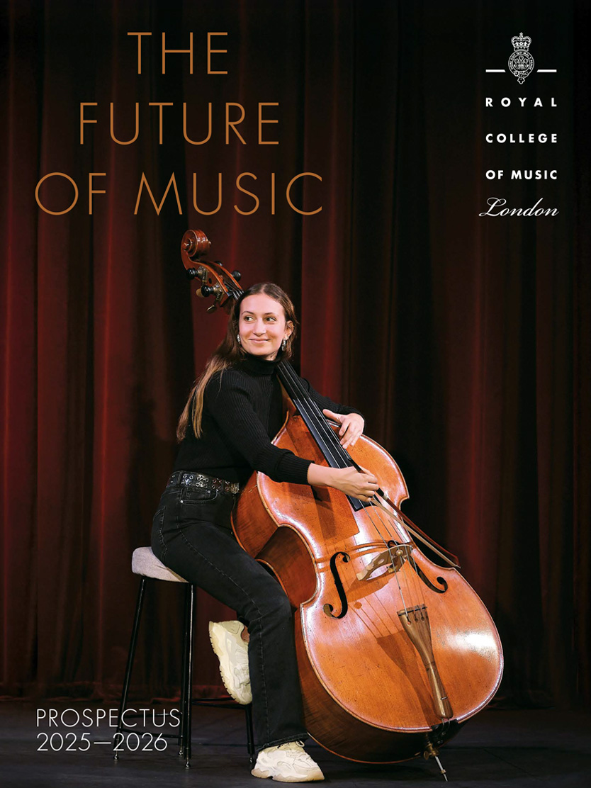 The front cover of the Prospectus 25-26 of a female cellist, wearing a black top and black trousers, looking beyond the stage smiling, with a red velvet curtain behind her.